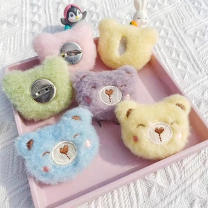 Close-up of colorful plush bear and heart brooches in a pink tray on white fabric