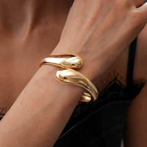 Close-up of a gold geometric crisscross cuff bracelet on a female wrist with lace details