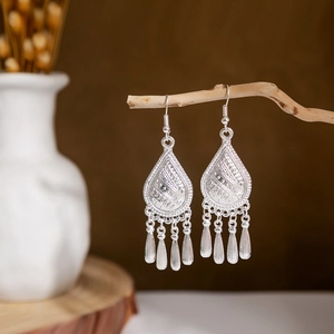 Close-up of ethnic silver hollow teardrop earrings with metal tassels on a branch