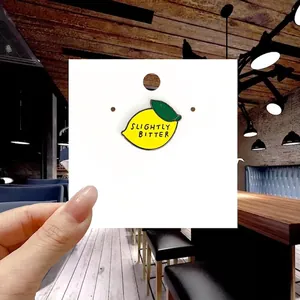 Detail of yellow lemon enamel pin with green leaf and Slightly Bitter text on card