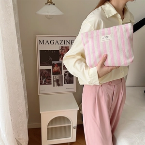 Model holding striped pink and white toiletry bag in a cozy home setting with magazines