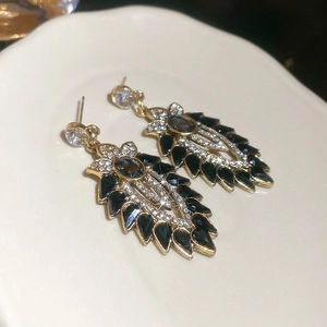Dettaglio di orecchini dorati vintage con foglie nere e accenti di cristallo lucido