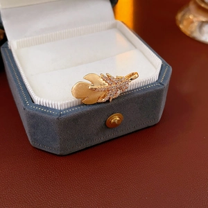 Macro shot of gold feather brooch with zircon inlays on a velvet jewelry box
