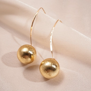 Macro detail of golden brushed metal spherical earrings with long elegant hooks