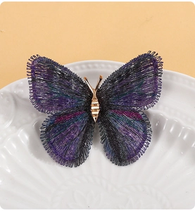 Gros plan sur une broche papillon brodée en dégradé avec des fils de soie métalliques