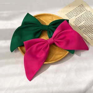 Detail of green and rose red fabric bow hair clips displayed on a rustic wooden plate