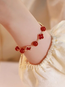 Macro shot of red agate beaded bracelet with gold clover pendant on a woman wrist