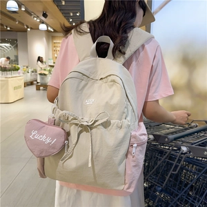 Chic beige and pink patchwork backpack with a bow and heart pendant in a daily setting