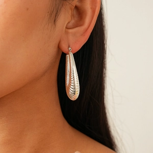Close-up of a silver teardrop earring featuring a ribbed texture on a model's ear