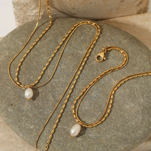 Double layered gold snake chain and pearl pendant necklace set on natural stone background
