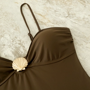Macro detail of dark brown swimwear featuring a decorative gold shell metal buckle