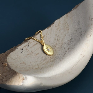 Gold starburst oval pendant necklace with sparkling zircon on textured beige background