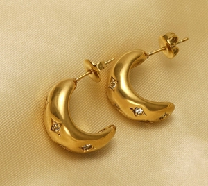 Macro shot of gold C-shaped earrings with inlaid zircons on a champagne silk fabric