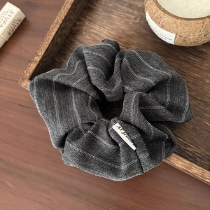 Detail of grey striped fabric hair scrunchie with soft cotton-linen texture on wooden tray
