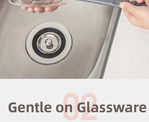 Detail showing long-handle silicone brush cleaning a glass cup inside a kitchen sink