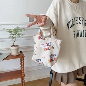 Close-up of beige corduroy tote bag featuring Keep Smiling print and metal snap button