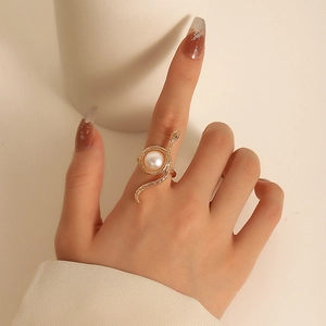 Gold snake ring wrapped around a white pearl on a model hand with minimalist background