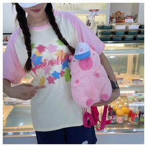Pink plush pig backpack with blue cap and woven strap shown in a lifestyle setting
