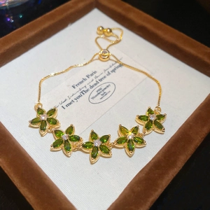 Macro detail of gold flower bracelet with green marquise stones and adjustable bead clasp