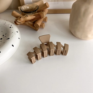 Close-up of matte khaki hair claw clip on white surface with cozy home decor background