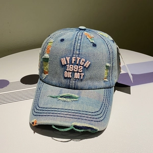 Close-up of pink 3D embroidery and distressed ripped details on blue denim baseball cap