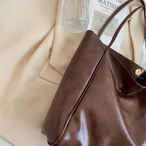 Grand cabas en cuir marron présenté sur un blazer beige dans un décor artistique