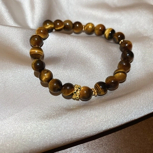 Detail of tiger eye bead bracelet with golden hollow charm on light silk background