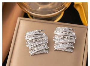 Macro detail of silver abstract earrings with textured wave patterns and metallic finish