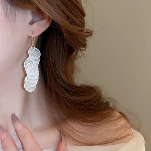 Close-up of elegant shell-like sequin tassel earrings worn by a model for a summer look