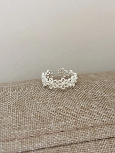Macro shot of silver open ring with hollow flower patterns on textured fabric