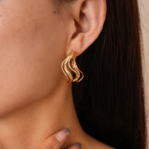 Close-up of golden irregular wave earrings showing polished metallic texture on a model