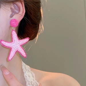 Close-up of pink raffia starfish earrings worn by a model for a beach vacation look