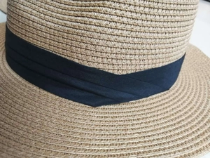 Detail of hand-woven straw sun hat texture featuring a black pleated ribbon decoration