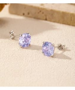 Close-up of silver stud earrings featuring large round faceted purple gemstones in a four-prong setting