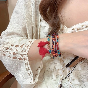 Detail of bohemian multilayer beaded bracelet featuring red tassel and colorful crystals