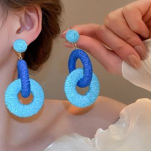 Detail of blue woven raffia earrings with golden metal studs on a model's ear