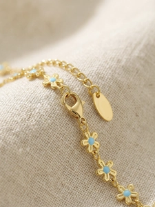 Macro detail of gold flower bracelet with blue enamel petals and lobster clasp closure