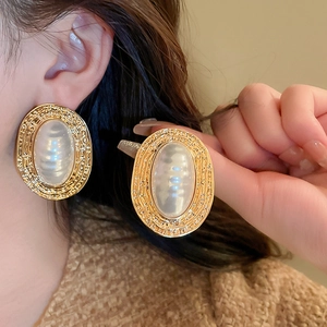 Macro shot of oversized vintage oval pearl earrings with textured golden metal frames