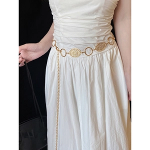 Detail of vintage gold metal chain belt with engraved oval medallions on a white dress