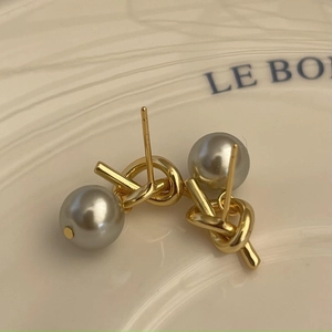 Macro shot of gold knot earrings with grey pearls on minimalist ceramic plate