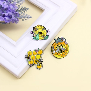Three enamel bee and honeycomb pins with intricate floral details on a beige backdrop