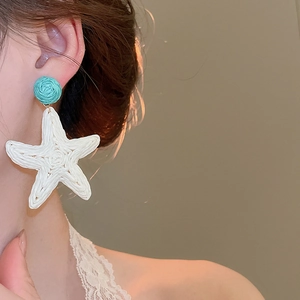Detailed close-up of woven raffia starfish earrings in blue and white on a model