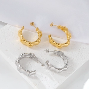 Bamboo style C-shaped stud earrings in gold and silver finish on white stone surface