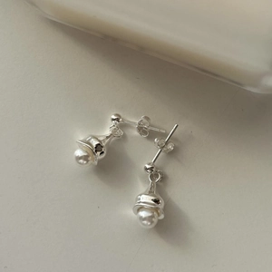 Macro shot of minimalist sterling silver pearl earrings on a clean beige surface