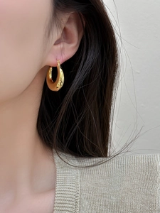 Close-up of elegant gold polished hoop earrings worn with minimalist knitwear detail