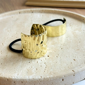 Detail of golden wave texture and smooth metallic hair cuffs on beige stone tray