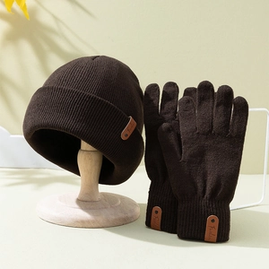 Deep brown knitted beanie and gloves set with fashion leather labels on beige background