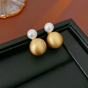 Detail of matte gold round beads and white pearl earrings on a black leather tray