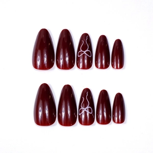 Glossy burgundy almond press-on nails with white bow designs on white background