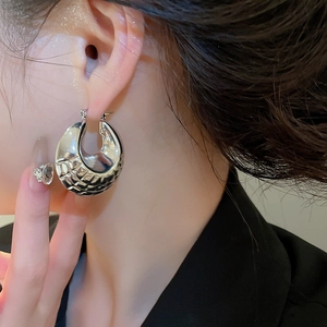 Detail of silver geometric hoop earring with textured weave pattern on model